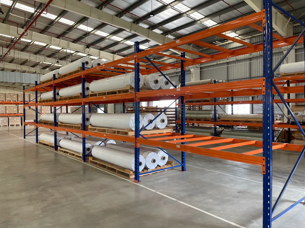 Dãy kệ pallet dài trong trung tâm phân phối mái cao, lối đi thẳng