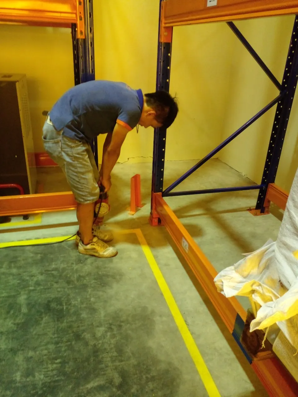 Kỹ thuật viên lắp tấm bảo vệ chân cột kệ tại khu vực có vạch sơn vàng