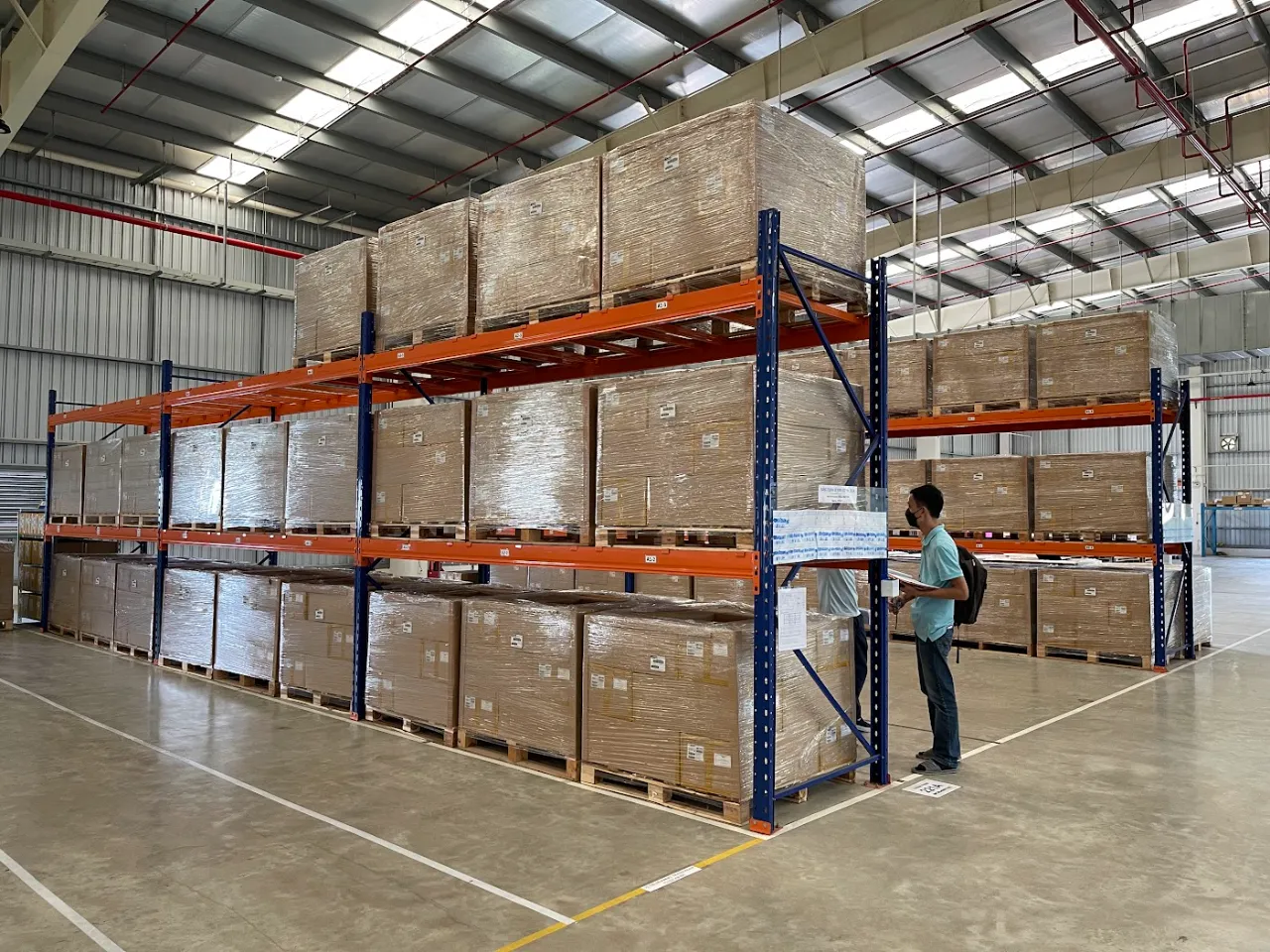 Nhân viên kiểm tra hàng thùng trên kệ pallet selective trong trung tâm phân phối